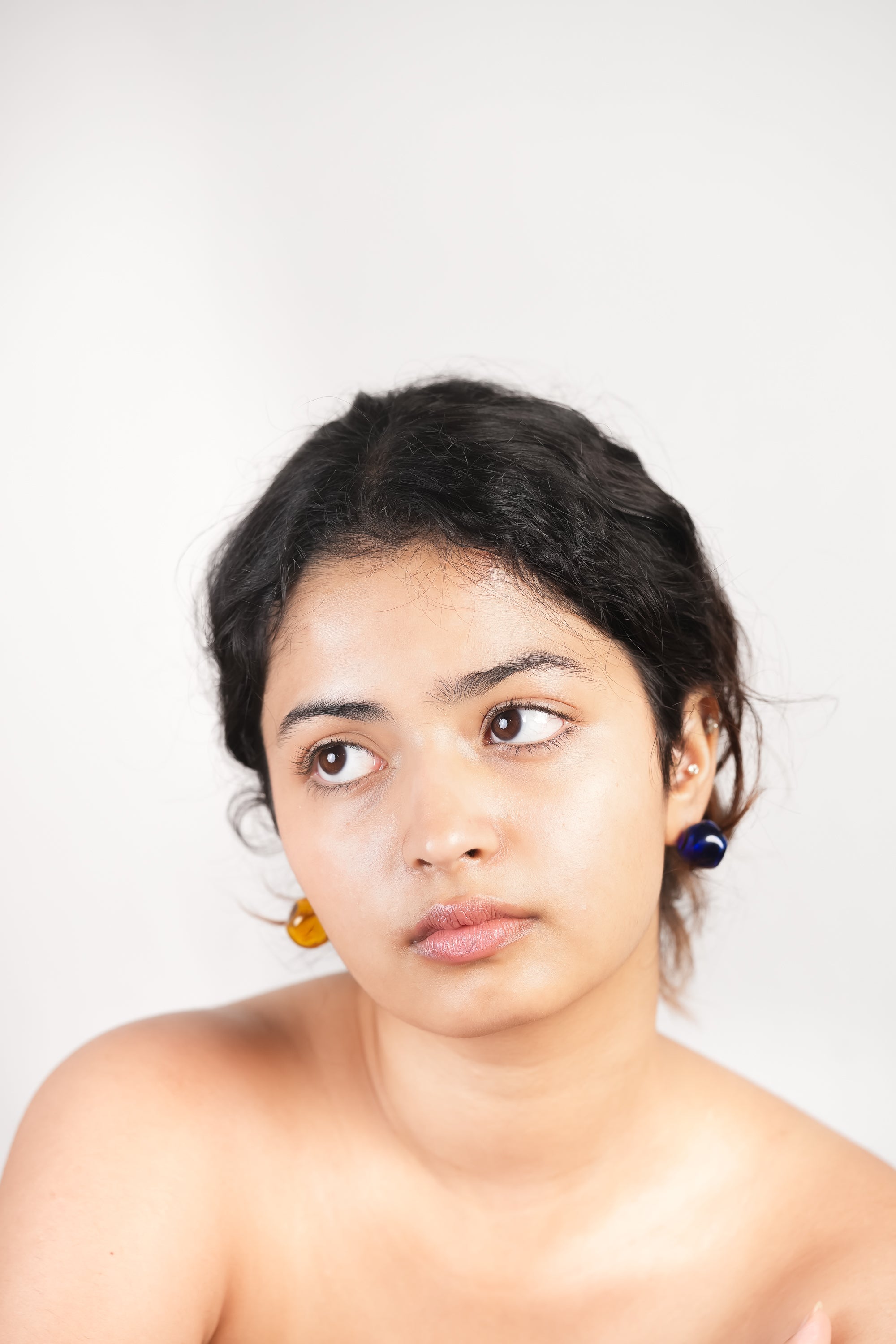 Model wearing handmade borosilicate glass mismatched hoops in blue and amber by AIROKAD STUDIO.