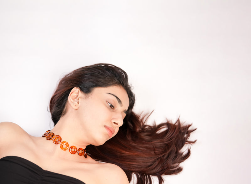 Woman with flowing hair wearing an brown hollow circles glass choker against a white background