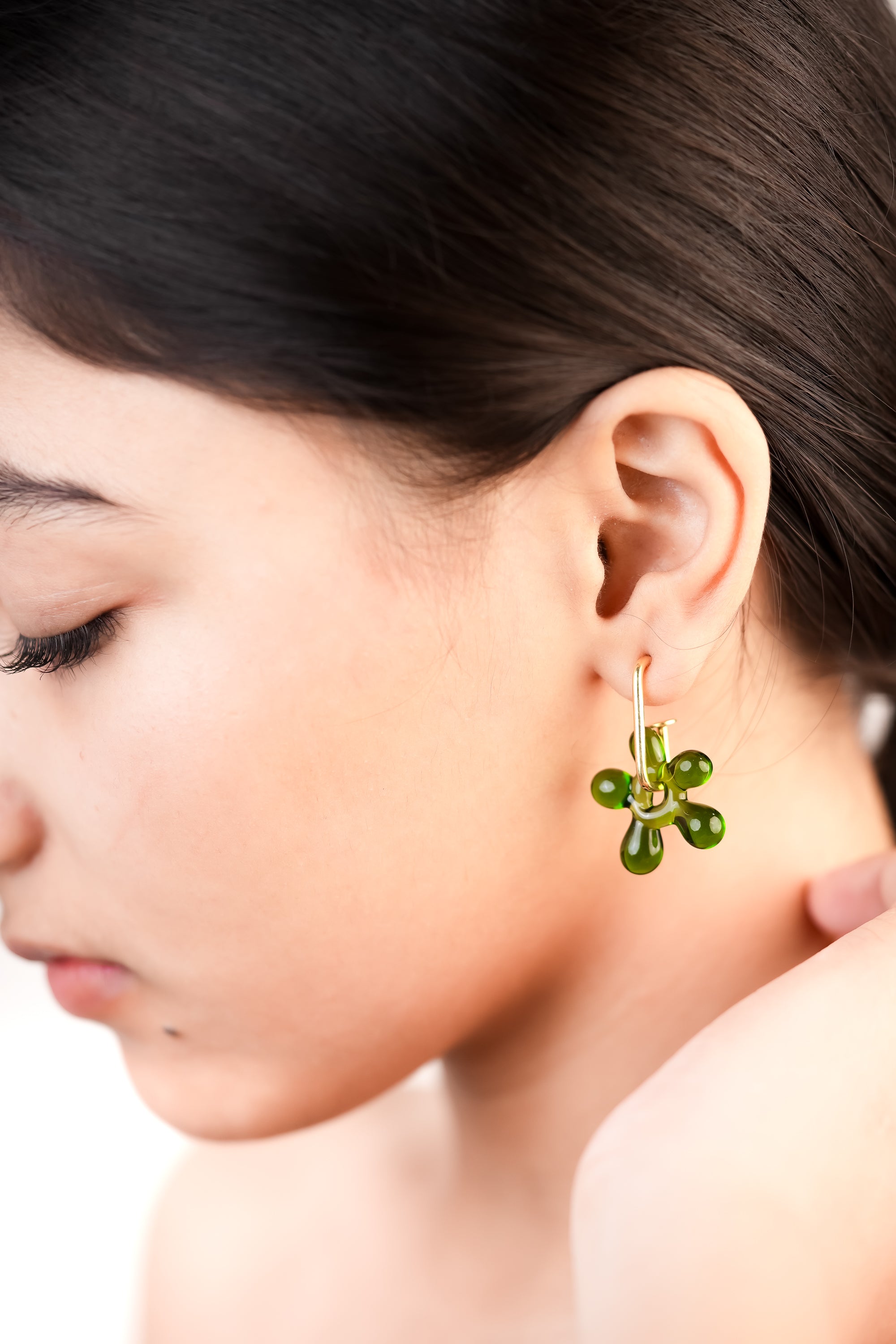 Model wearing handcrafted borosilicate glass blossom hoops in green by AIROKAD STUDIO.