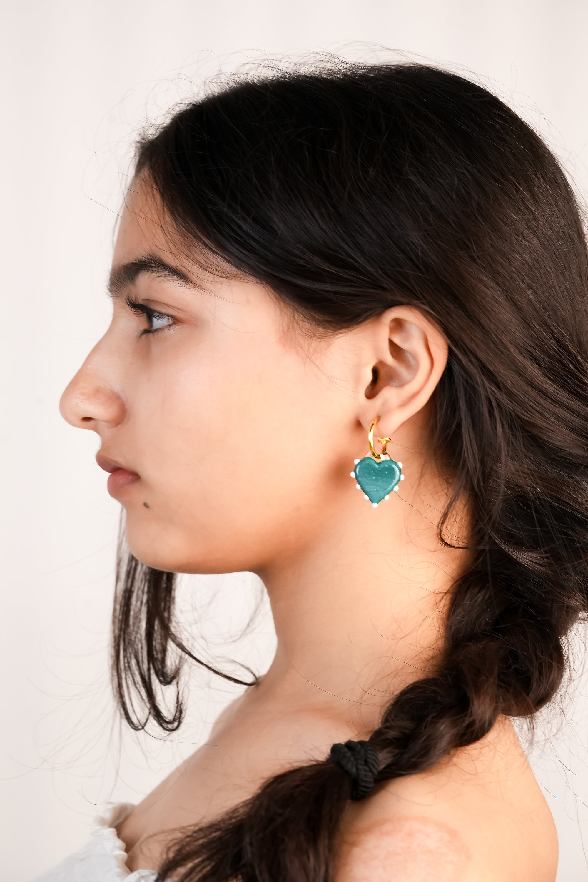 model wearing borosilicate glass handcrafted blue heart shaped hoops with white dot detailing by AIROKAD STUDIO.