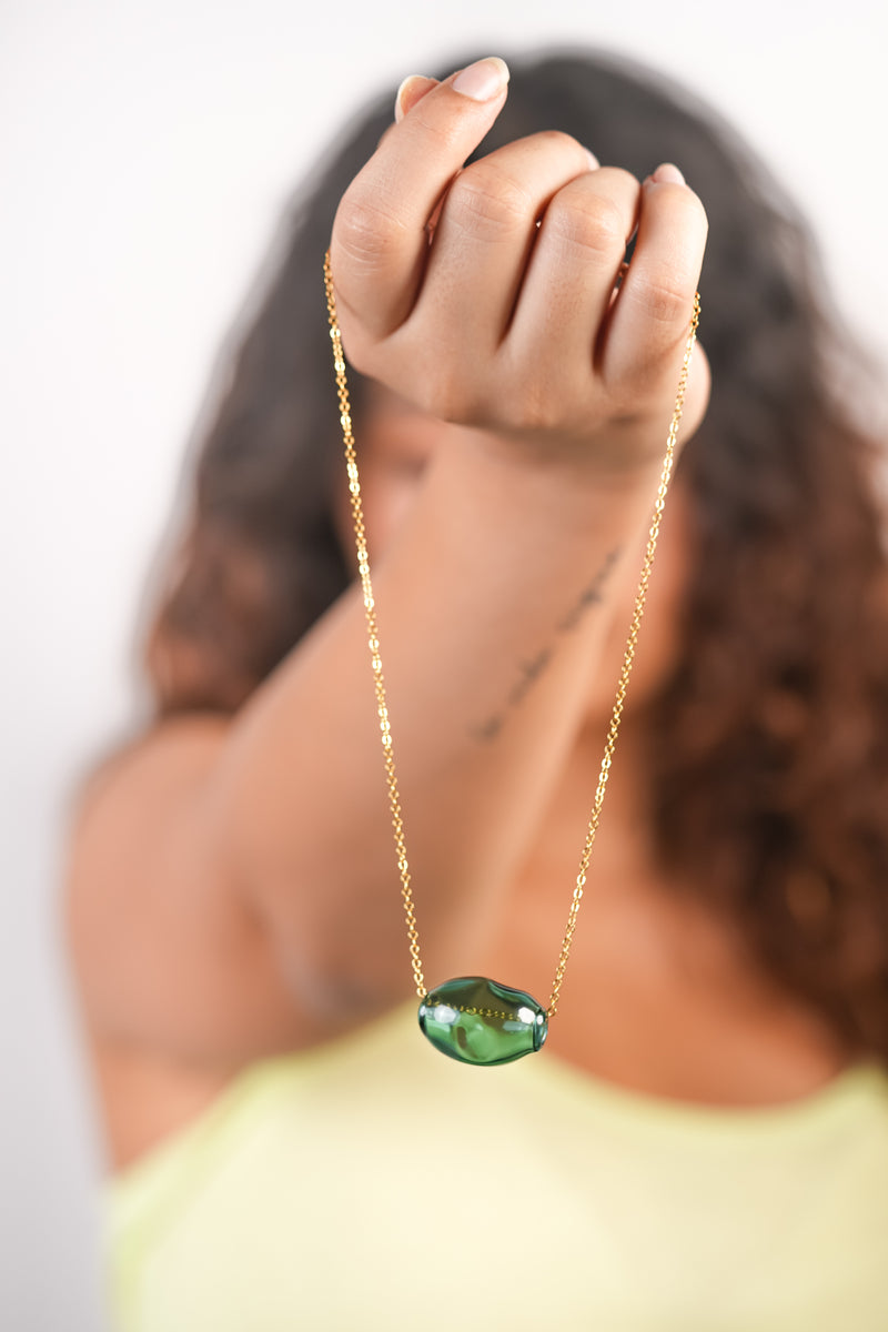 Model holding handmade borosilicate glass bubble necklace in teal with golden chain by AIROKAD STUDIO. 