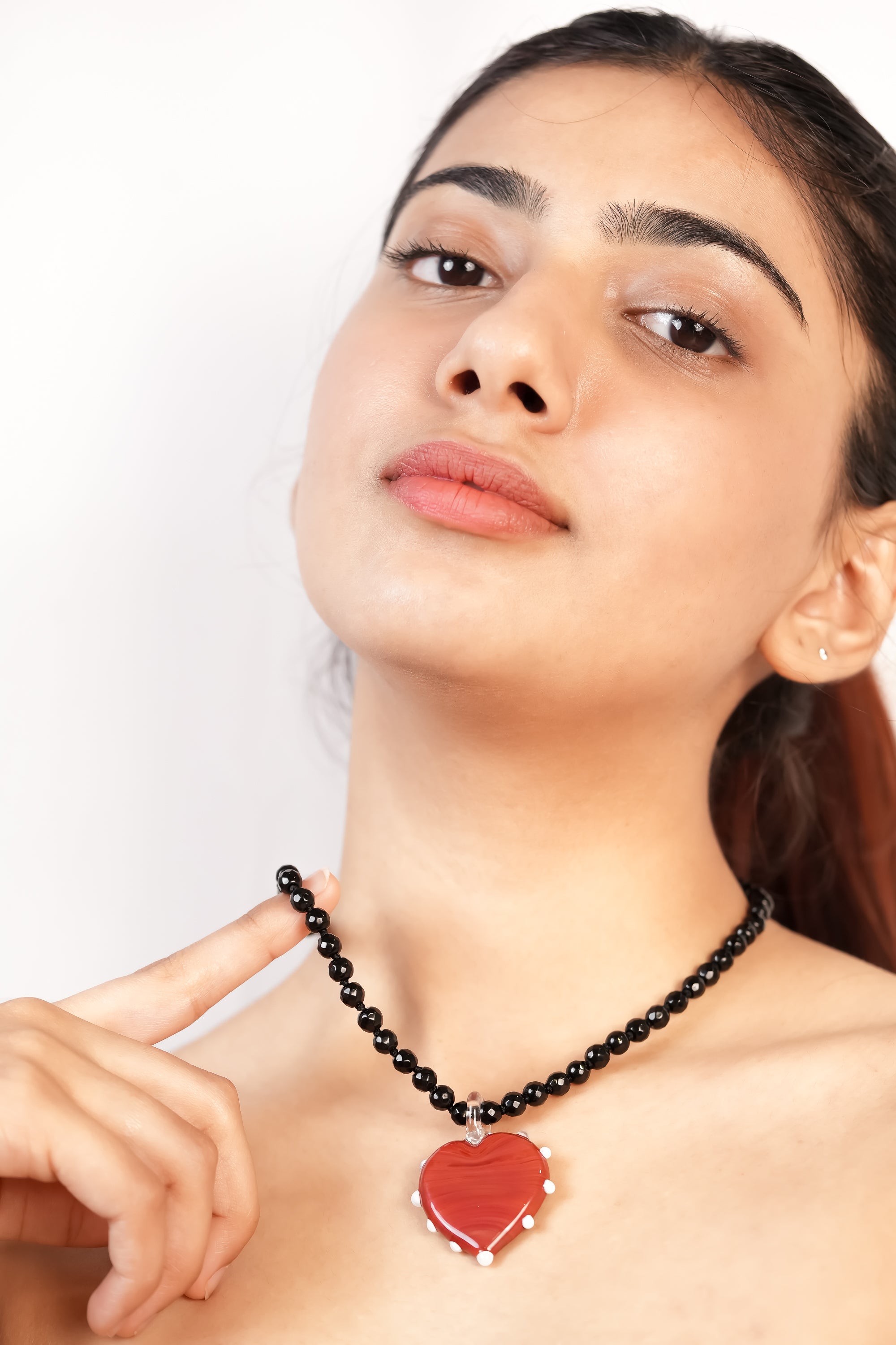 model wearing handcrafted borosilicate glass red heart pendant with lining and white dot detailing and black jade beads chain by AIROKAD STUDIO.