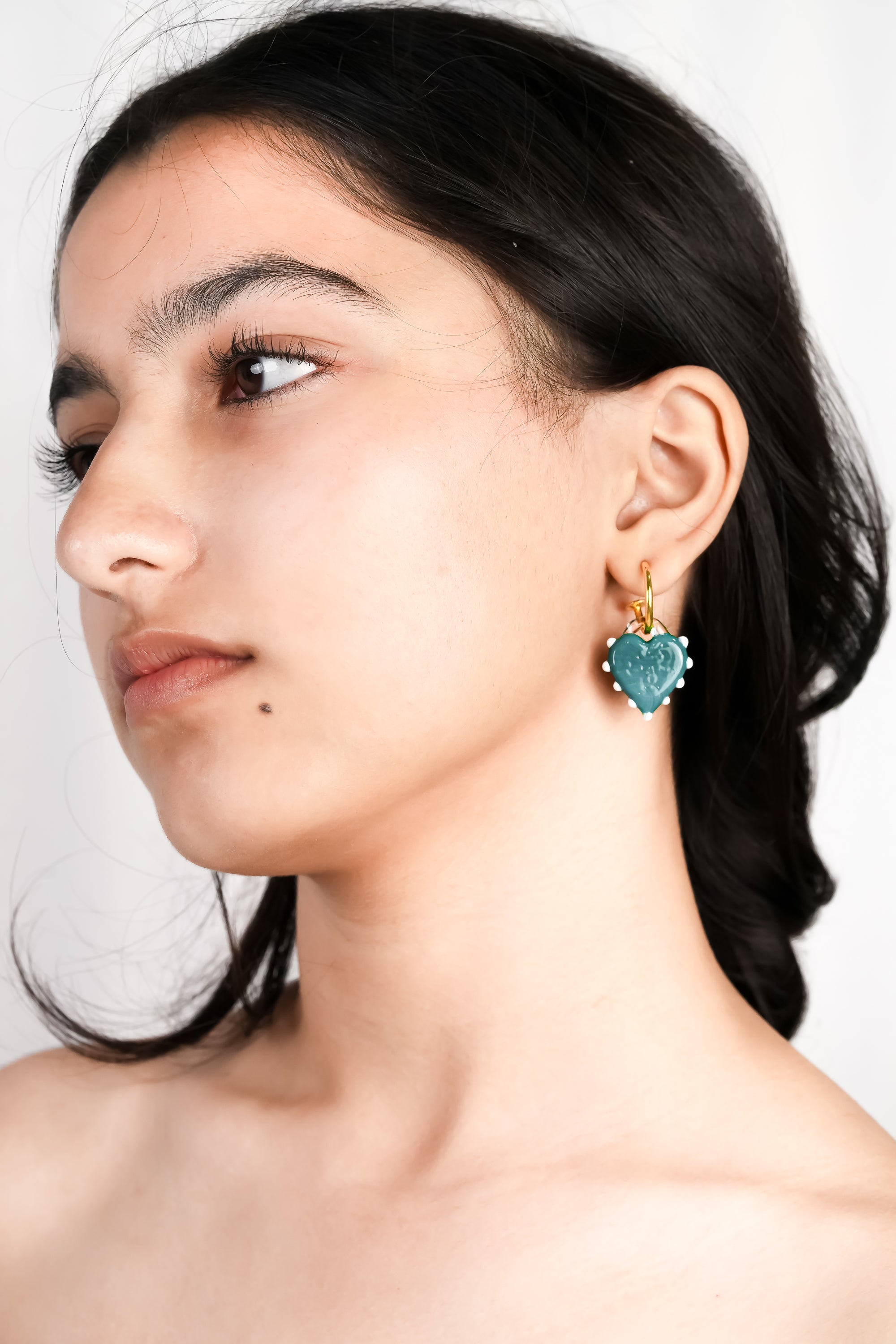 model wearing handcrafted borosilicate glass turquoise hoops in heart shape by AIROKAD STUDIO.